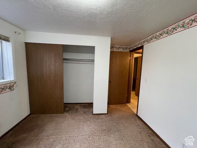 Unfurnished bedroom with a closet, a textured ceiling, and light carpet