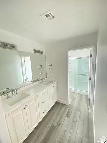Bathroom featuring wood-type flooring, an enclosed shower, and double sink vanity