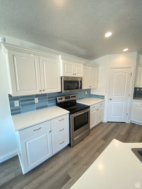 Kitchen featuring dark hardwood / wood-style floors, white cabinets, stainless steel appliances, and backsplash