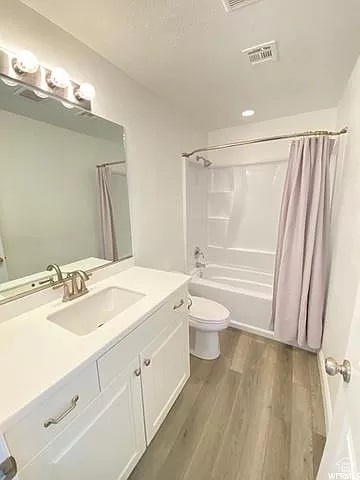 Full bathroom with wood-type flooring, toilet, shower / bathtub combination with curtain, and large vanity