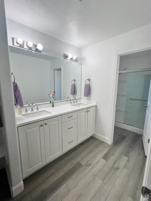 Bathroom featuring hardwood / wood-style floors, a textured ceiling, dual vanity, and walk in shower