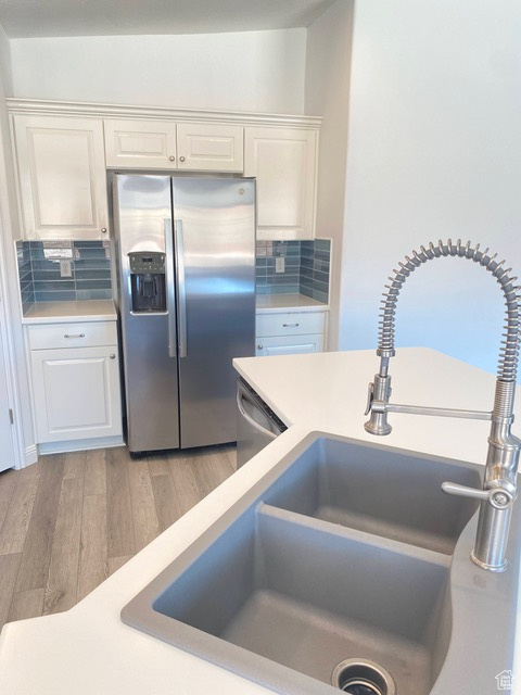 Kitchen with white cabinets, stainless steel appliances, tasteful backsplash, and light hardwood / wood-style flooring