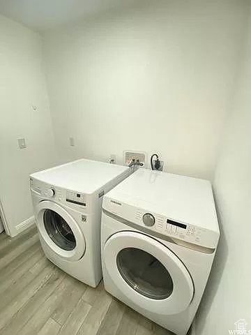 Washroom with washer hookup, light wood-type flooring, hookup for an electric dryer, and washing machine and dryer