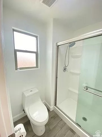 Bathroom with a shower with shower door, toilet, and wood-type flooring