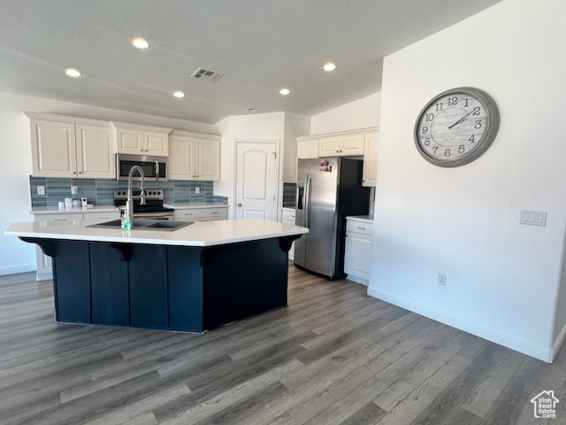 Kitchen featuring dark hardwood / wood-style flooring, white cabinetry, appliances with stainless steel finishes, and an island with sink