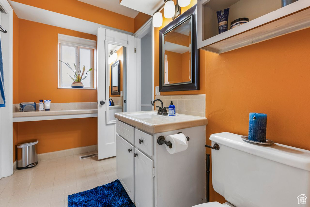 Bathroom with backsplash, toilet, tile flooring, and vanity with extensive cabinet space