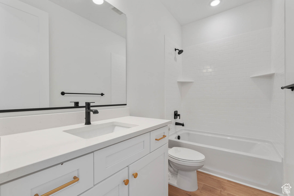 Full bathroom featuring vanity, tiled shower / bath combo, toilet, and hardwood / wood-style floors