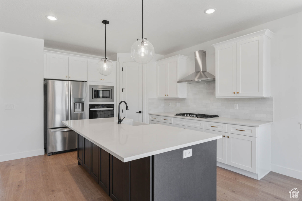 Kitchen with tasteful backsplash, wall chimney range hood, light wood-type flooring, sink, and appliances with stainless steel finishes