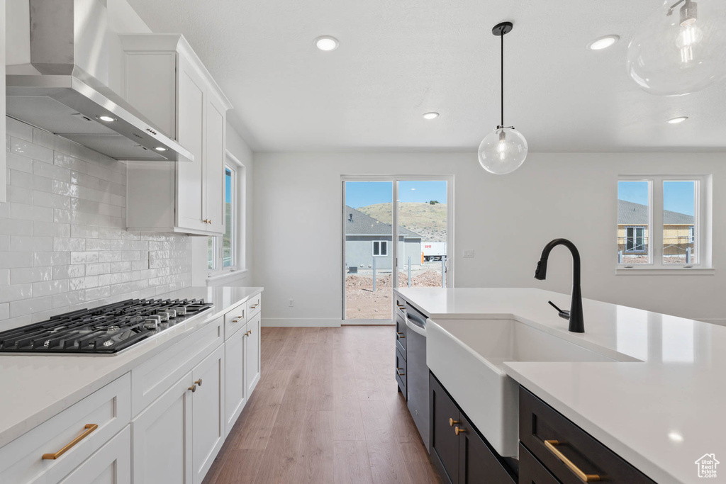 Kitchen with light wood-type flooring, wall chimney range hood, white cabinets, stainless steel appliances, and decorative backsplash