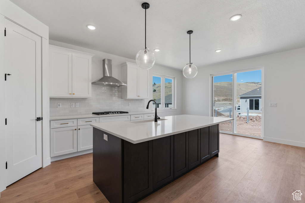 Kitchen with wall chimney range hood, white cabinets, sink, light hardwood / wood-style flooring, and backsplash