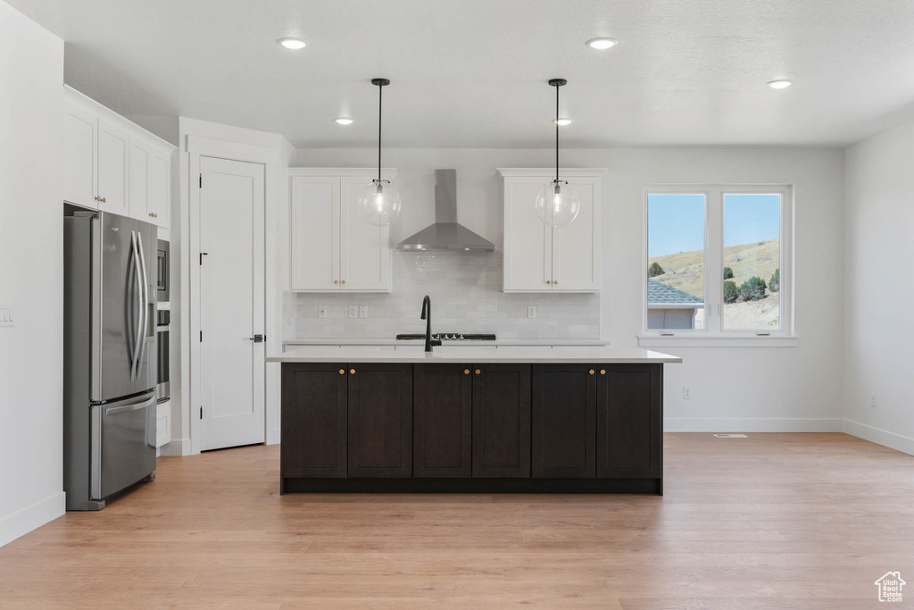 Kitchen featuring stainless steel fridge, pendant lighting, backsplash, light wood-type flooring, and wall chimney exhaust hood