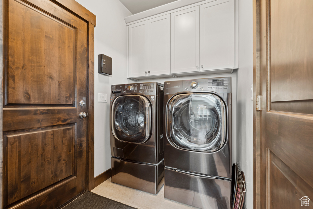 Clothes washing area with light tile floors, washer and dryer, and cabinets