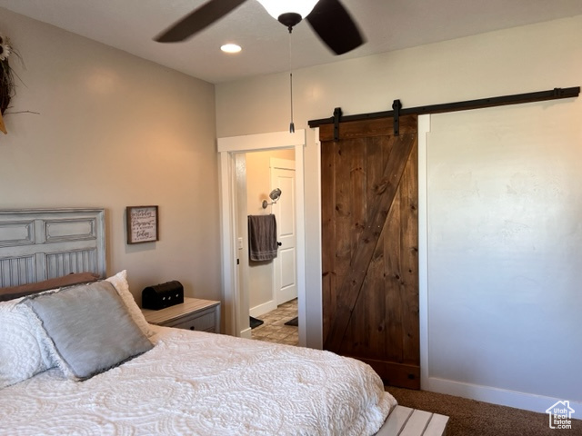 Carpeted bedroom with a barn door and ceiling fan