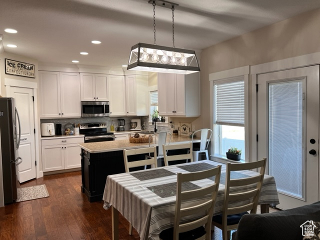 Kitchen featuring dark hardwood flooring, white cabinets, appliances with stainless steel finishes, tasteful backsplash, and decorative light fixtures