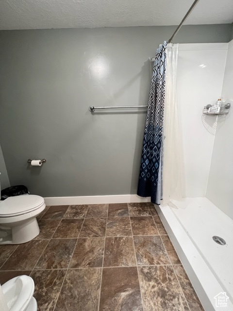 Bathroom with a textured ceiling, toilet, a shower with shower curtain, and tile flooring