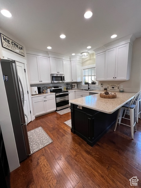 Kitchen featuring kitchen peninsula, dark hardwood flooring, white cabinets, and a kitchen bar
