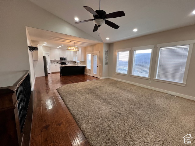 Unfurnished living room featuring dark hardwood / wood-style flooring, ceiling fan with notable chandelier, and vaulted ceiling
