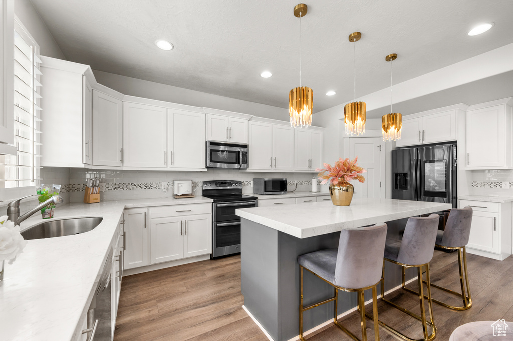 Kitchen with white cabinets, pendant lighting, tasteful backsplash, light hardwood / wood-style floors, and stainless steel appliances