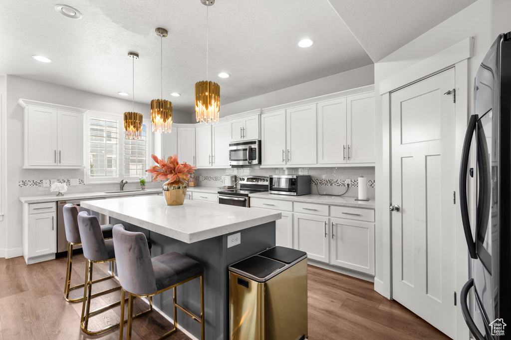 Kitchen featuring white cabinetry, a center island, decorative light fixtures, wood-type flooring, and stainless steel appliances