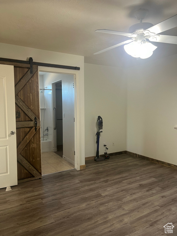 Spare room with dark hardwood / wood-style flooring, a barn door, and ceiling fan
