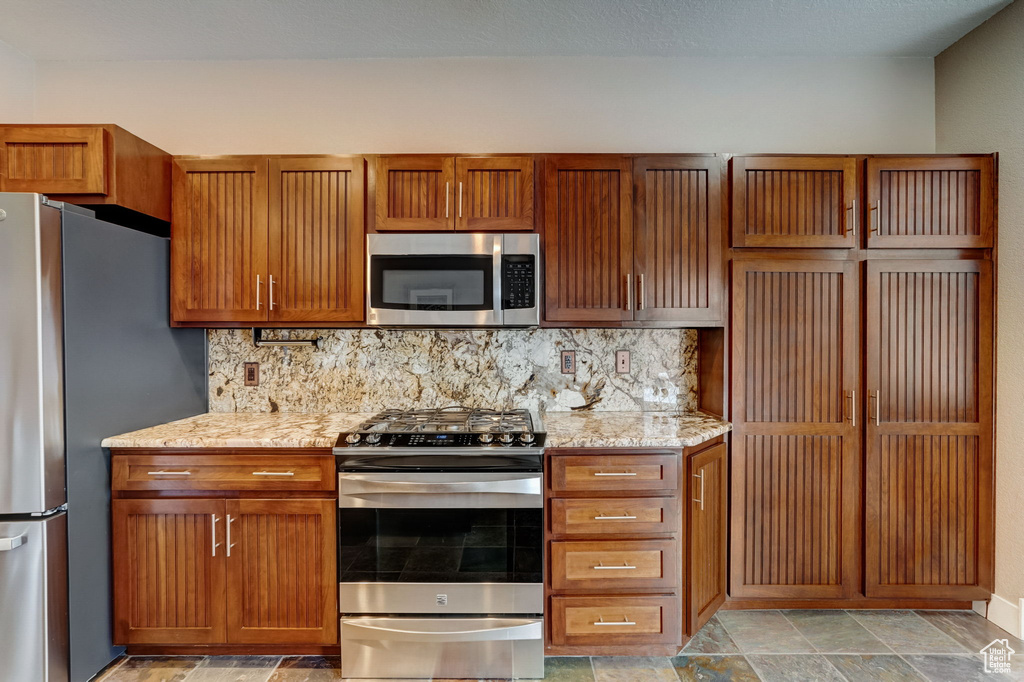 Kitchen featuring backsplash, light tile flooring, stainless steel appliances, and light stone countertops