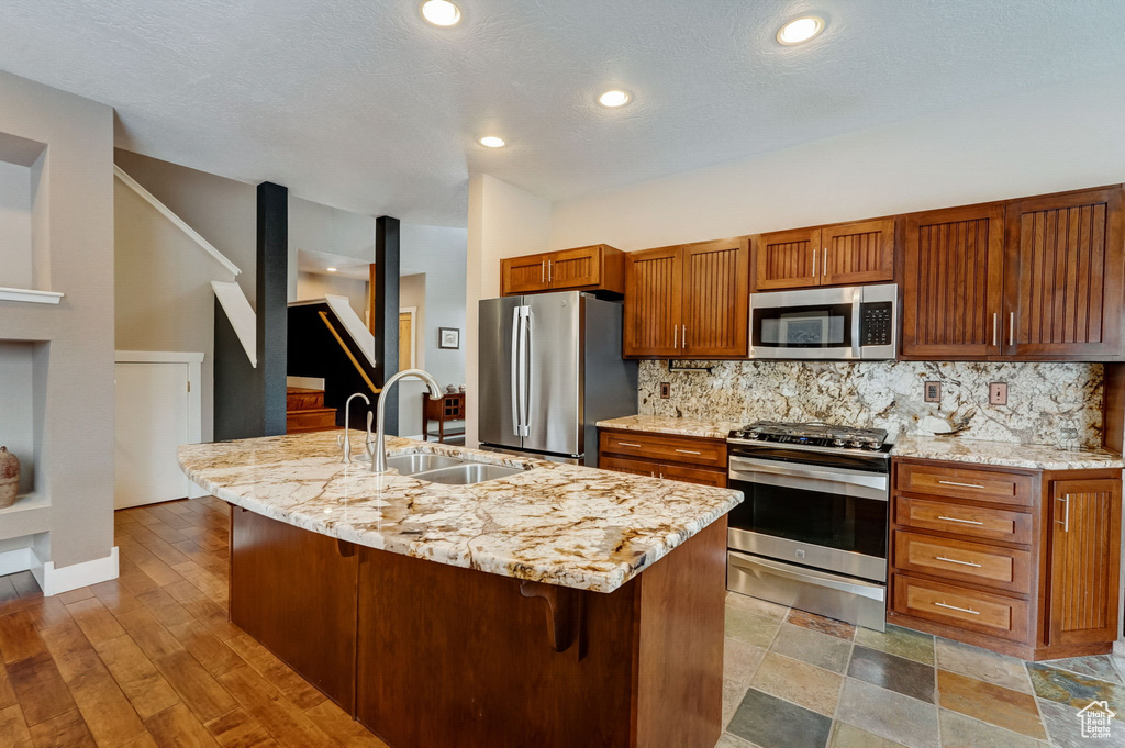 Kitchen with a kitchen island with sink, sink, light hardwood / wood-style floors, backsplash, and appliances with stainless steel finishes
