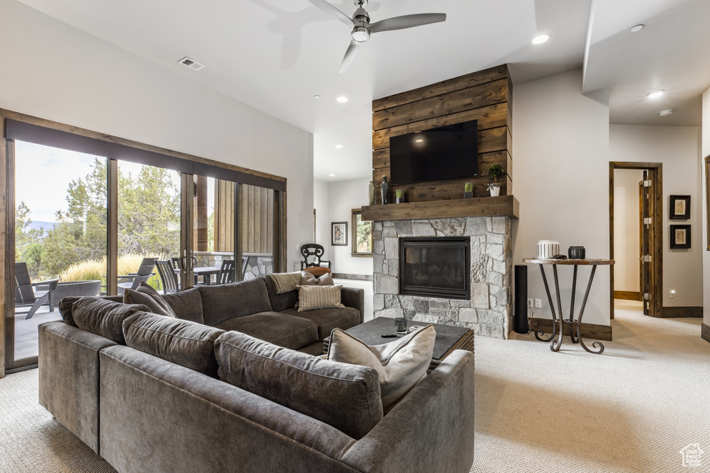 Carpeted living room featuring a stone fireplace and ceiling fan