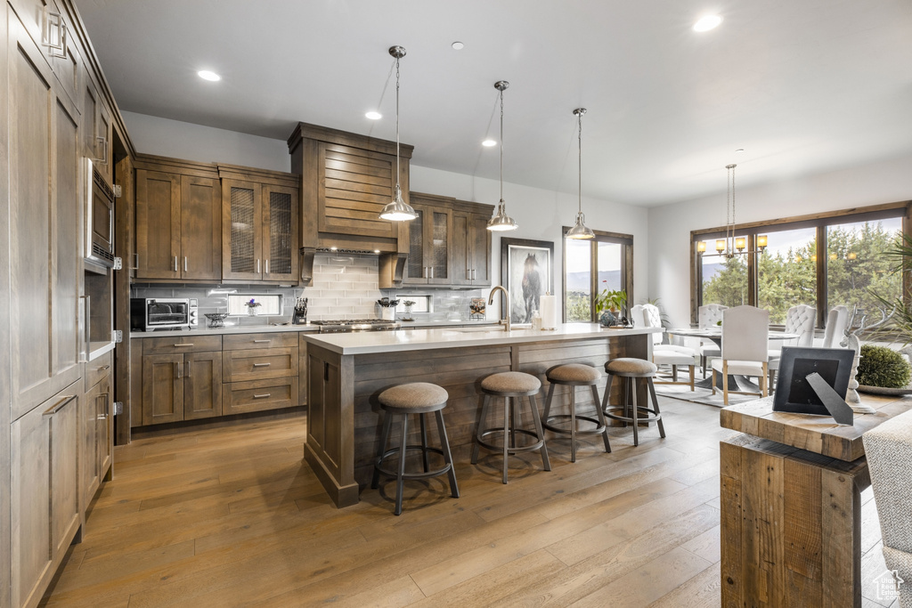 Kitchen featuring a center island with sink, tasteful backsplash, hanging light fixtures, and light hardwood / wood-style flooring