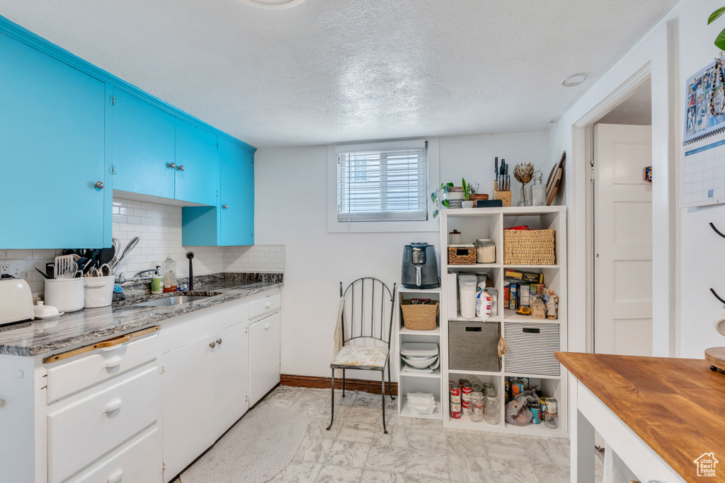 Kitchen with a textured ceiling, tasteful backsplash, light tile flooring, blue cabinetry, and sink