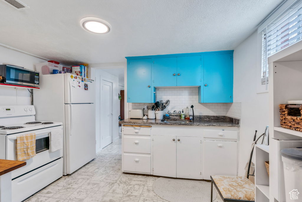 Kitchen featuring white appliances, light tile flooring, backsplash, blue cabinets, and white cabinets