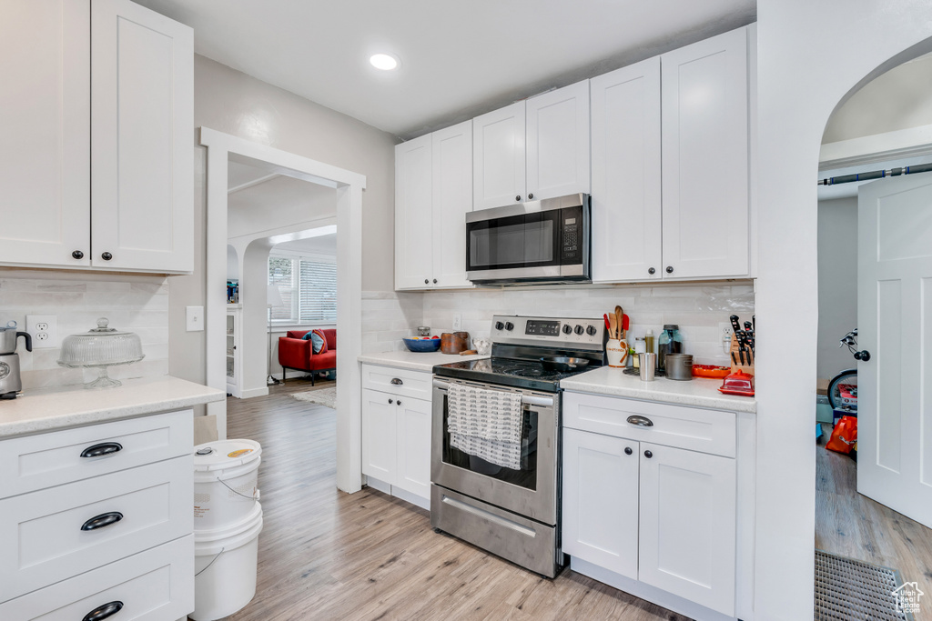 Kitchen featuring stainless steel appliances, tasteful backsplash, white cabinetry, and light hardwood / wood-style flooring