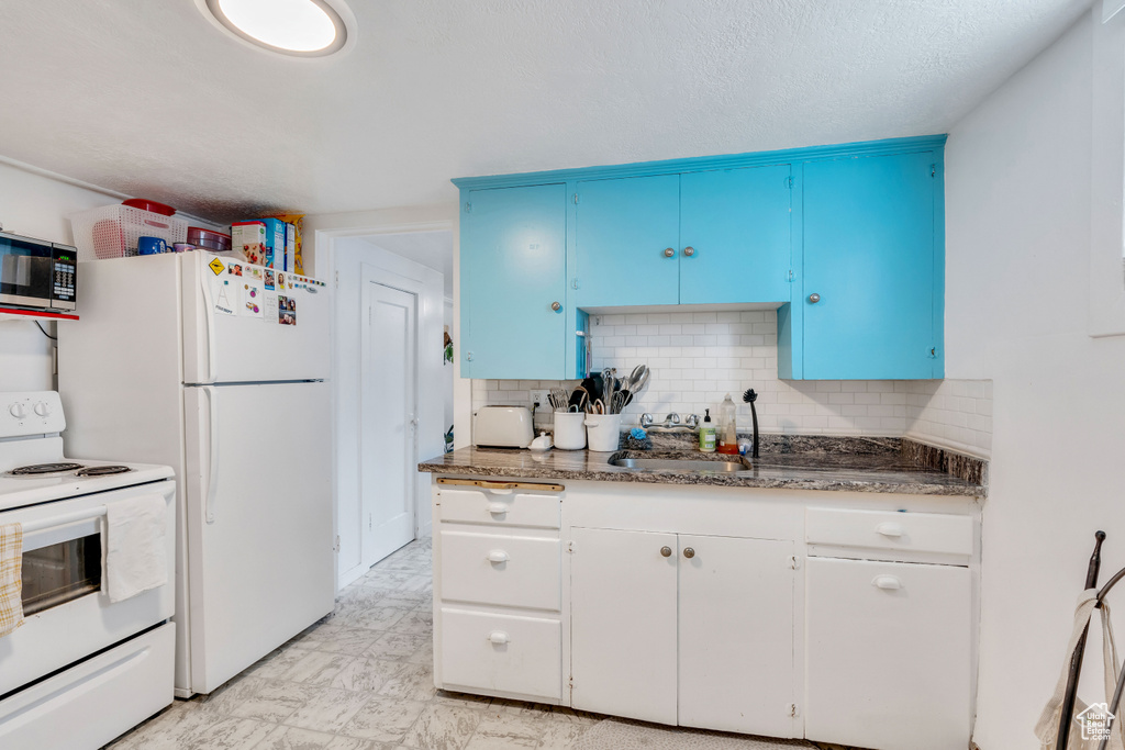 Kitchen with light tile flooring, white appliances, tasteful backsplash, dark stone countertops, and blue cabinetry