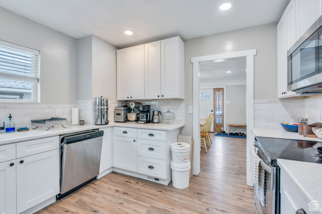 Kitchen featuring backsplash, stainless steel appliances, light hardwood / wood-style floors, white cabinetry, and a healthy amount of sunlight