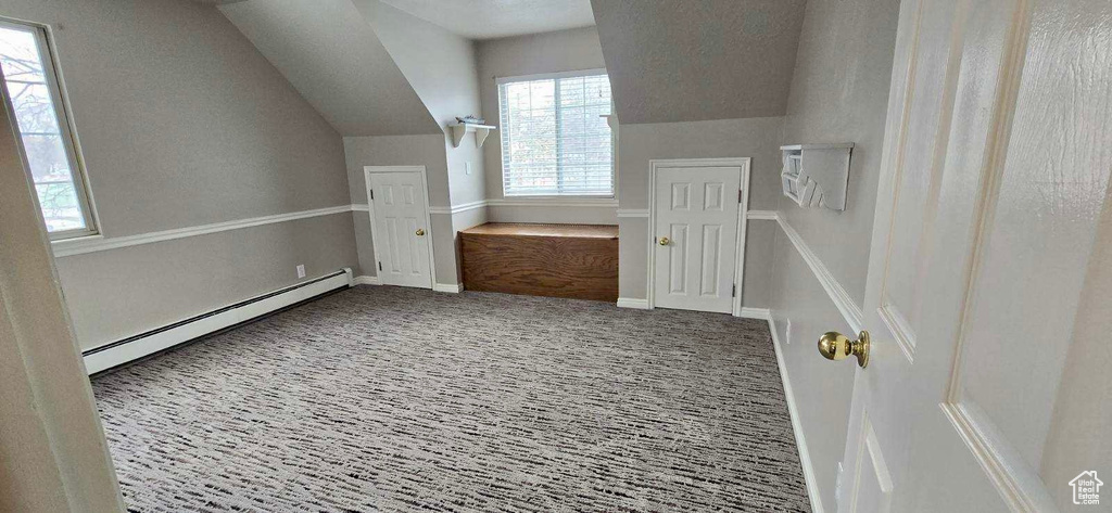 Additional living space with a baseboard heating unit, vaulted ceiling, and carpet floors