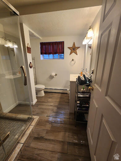 Bathroom with hardwood / wood-style floors, baseboard heating, walk in shower, toilet, and vanity