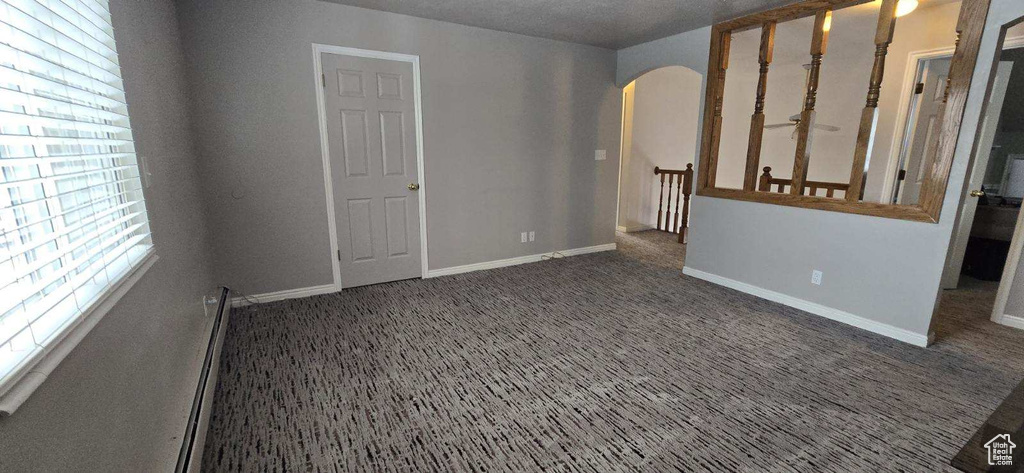 Empty room with dark carpet, a healthy amount of sunlight, and a baseboard heating unit