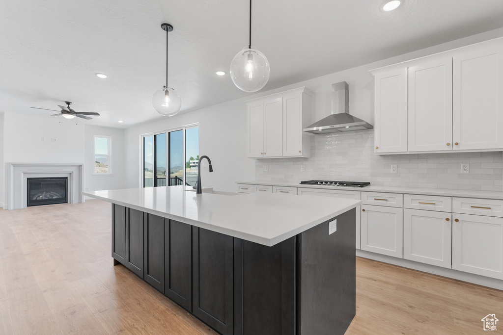 Kitchen featuring tasteful backsplash, wall chimney range hood, white cabinets, light hardwood / wood-style flooring, and gas stovetop