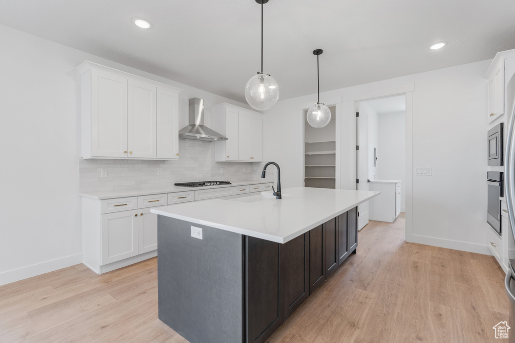 Kitchen with white cabinetry, light hardwood / wood-style floors, appliances with stainless steel finishes, wall chimney exhaust hood, and decorative backsplash