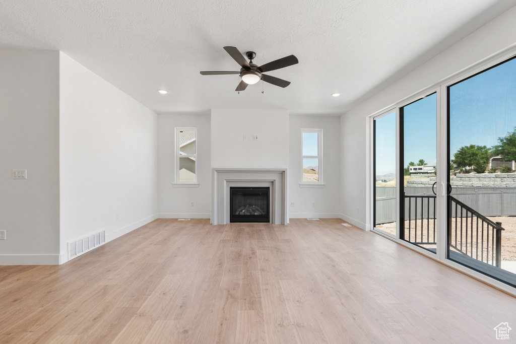 Unfurnished living room featuring light wood-type flooring, ceiling fan, and a textured ceiling