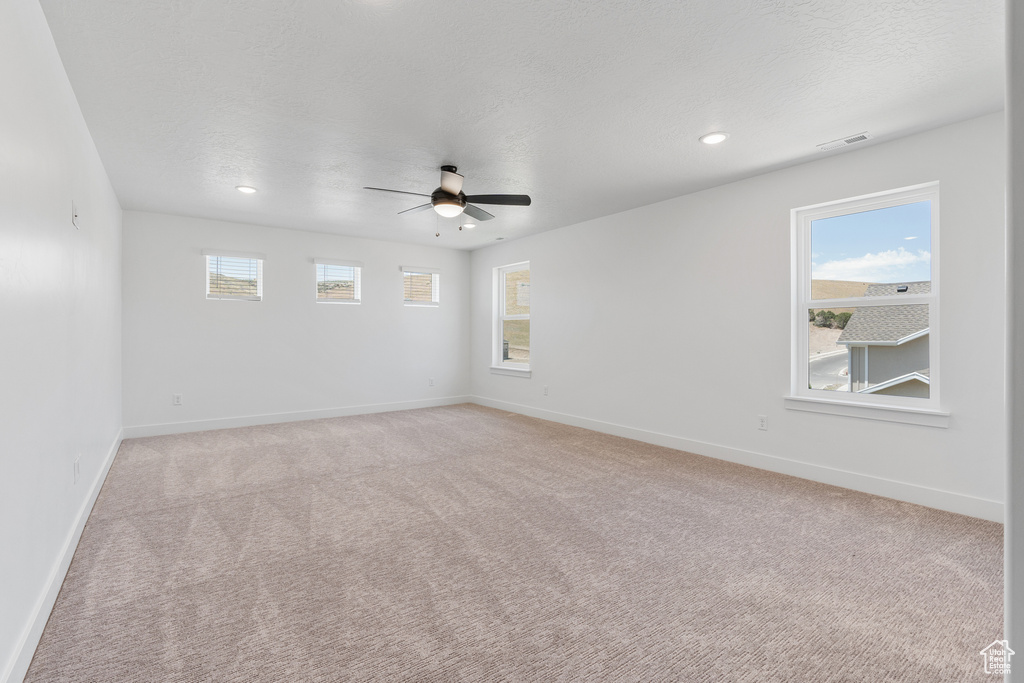 Carpeted spare room featuring a healthy amount of sunlight and ceiling fan
