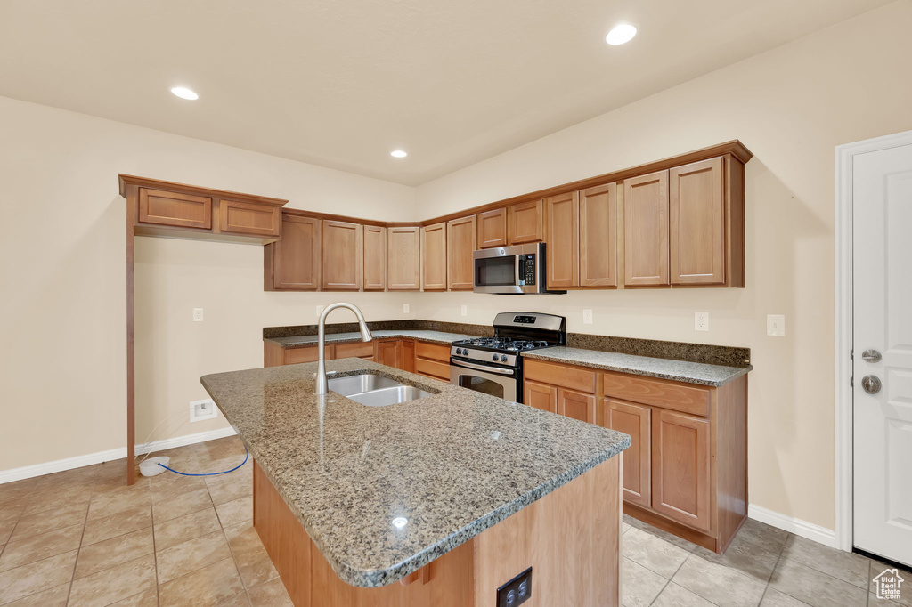 Kitchen with stone countertops, sink, appliances with stainless steel finishes, a center island with sink, and light tile floors