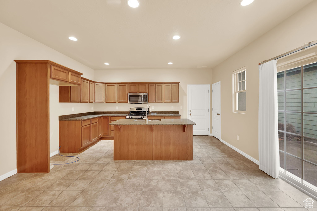 Kitchen featuring sink, light tile flooring, stainless steel appliances, and a center island with sink