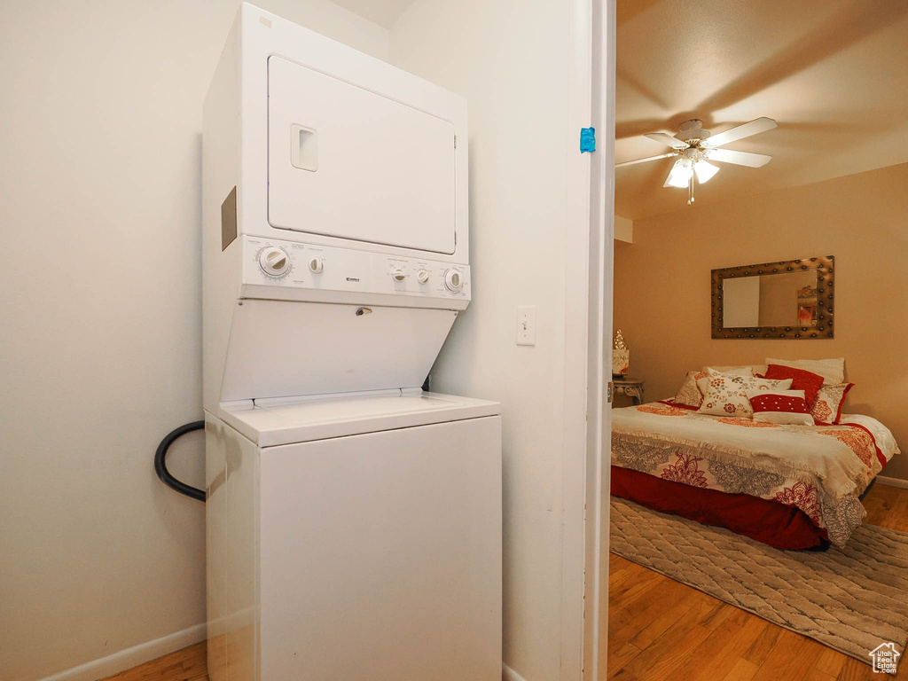 Laundry room with ceiling fan, stacked washing maching and dryer, and light hardwood / wood-style flooring