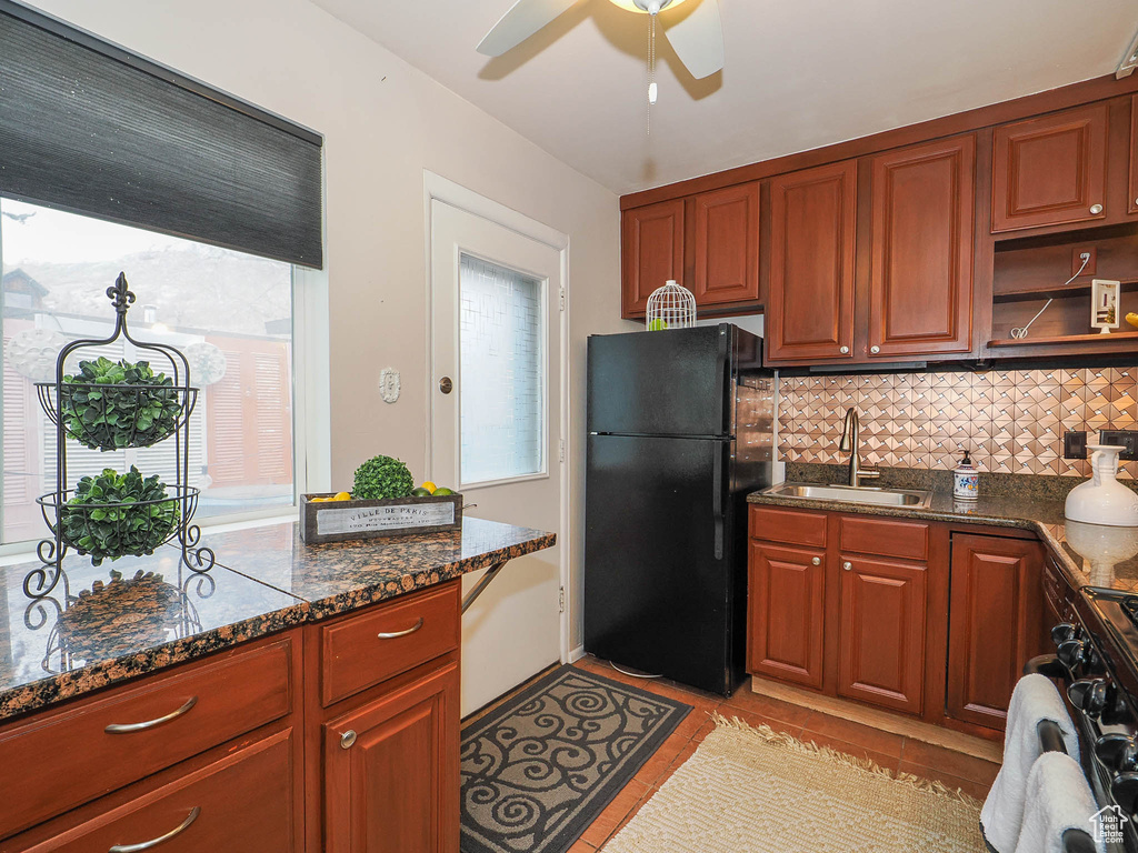 Kitchen with sink, tasteful backsplash, dark stone counters, black fridge, and ceiling fan