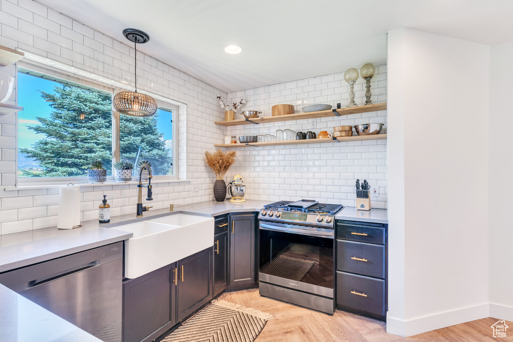 Kitchen featuring backsplash, stainless steel appliances, light parquet floors, sink, and hanging light fixtures