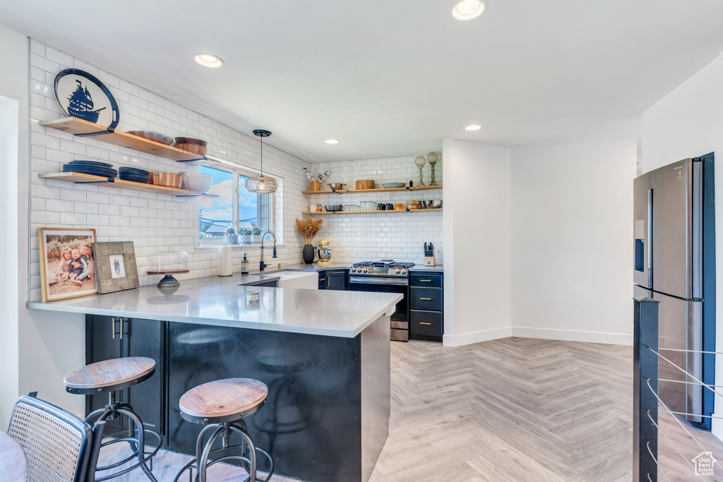 Kitchen featuring appliances with stainless steel finishes, light parquet flooring, sink, a breakfast bar, and decorative light fixtures