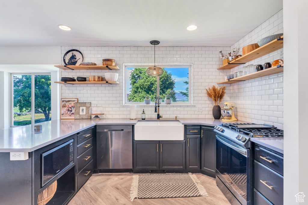 Kitchen with tasteful backsplash, kitchen peninsula, light parquet flooring, hanging light fixtures, and appliances with stainless steel finishes