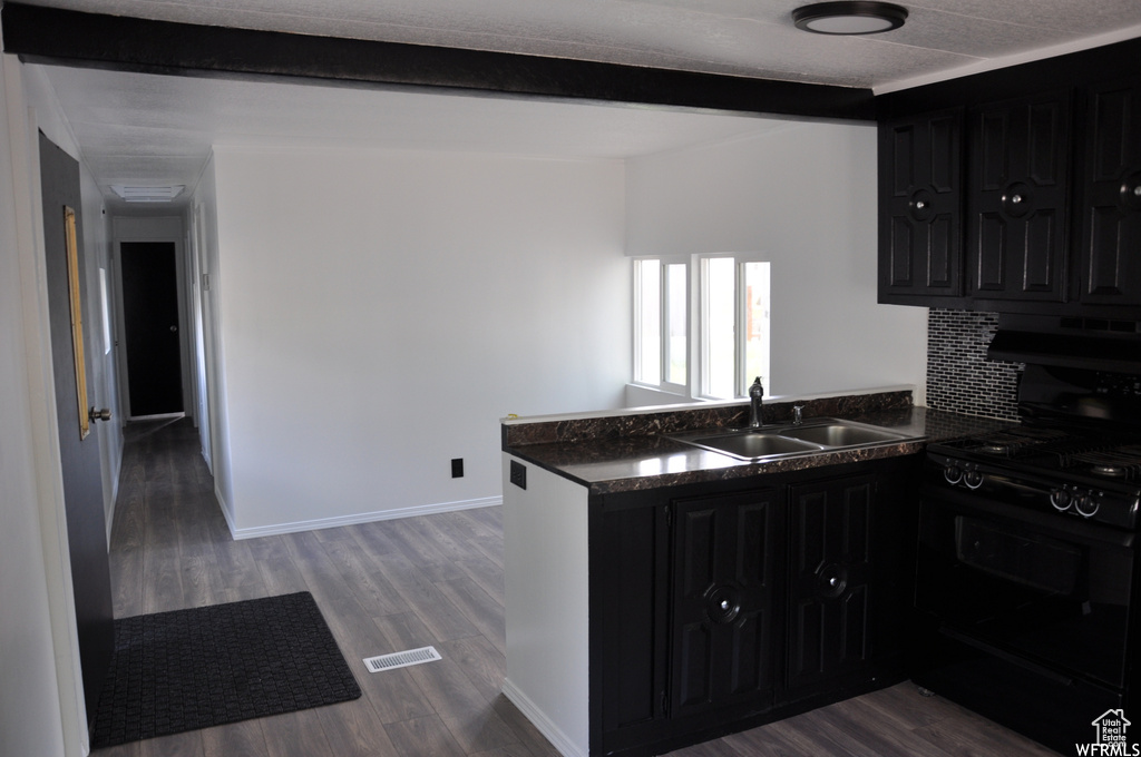 Kitchen featuring dark hardwood / wood-style flooring, kitchen peninsula, black stove, and sink