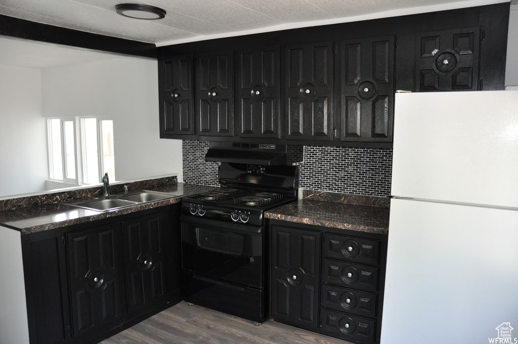Kitchen with tasteful backsplash, hardwood / wood-style floors, sink, white refrigerator, and black range oven