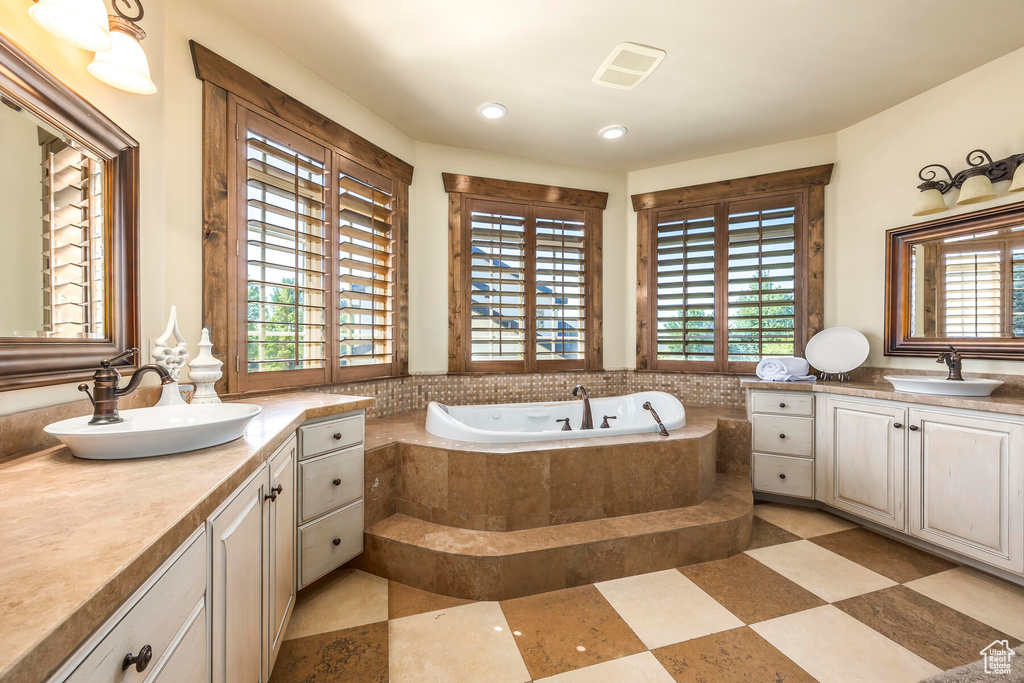 Bathroom with tile patterned flooring, a relaxing tiled tub, and vanity